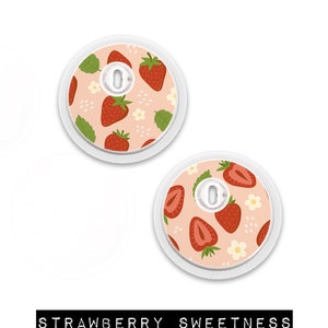 May include: Two round, white medical device covers with a strawberry pattern. The design features red strawberries, green leaves, and white flowers on a light pink background. The text "STRAWBERRY SWEETNESS" is at the bottom.