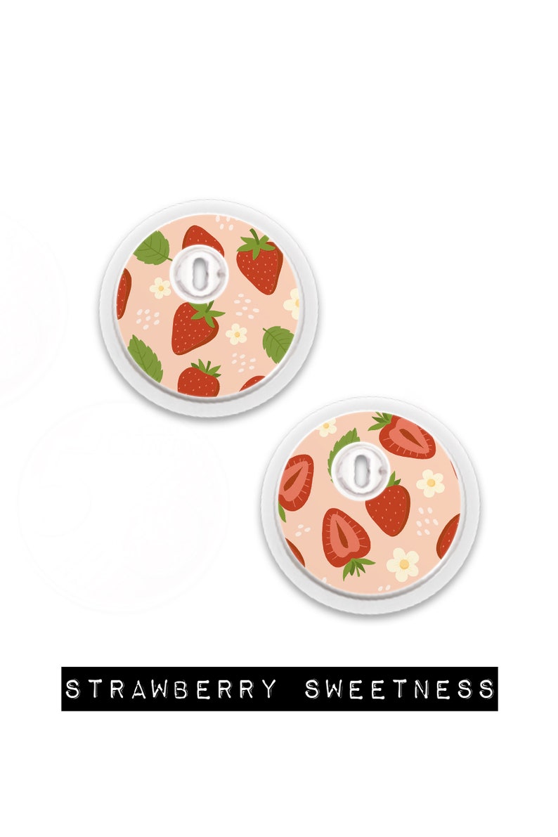 May include: Two round, white medical device covers with a strawberry pattern. The design features red strawberries, green leaves, and white flowers on a light pink background. The text "STRAWBERRY SWEETNESS" is at the bottom.