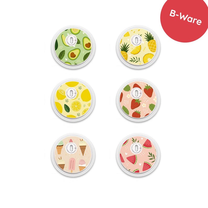 May include: A collection of six round, white medical device covers with colorful fruit and dessert patterns. Designs include avocados, pineapples, lemons, strawberries, ice cream cones, and watermelon slices. The covers have a small, central opening.