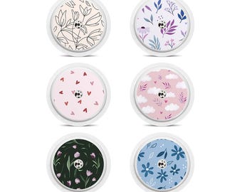 May include: Six round medical device covers with floral and patterned designs. The covers feature various patterns, including hearts, flowers, and leaves, in colors like pink, blue, and green. Each cover has a white border.