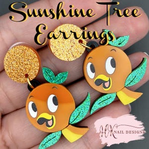May include: Orange bird earrings with green glitter accents and a gold glitter circle. The earrings have black hardware. The text "Sunshine Tree Earrings" is at the top of the image.