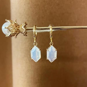 May include: A pair of gold hoop earrings with a white, faceted, geometric gemstone pendant.