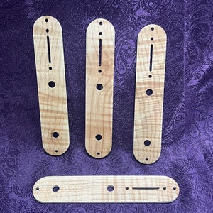 May include: Four wooden guitar pickguards with a natural wood grain finish. The pickguards have multiple holes for mounting screws and a single long slot for a pickup.