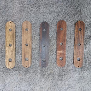 May include: Five elongated, rectangular wooden strips arranged vertically. Each piece features three circular holes aligned along the centre and two smaller holes at the top and bottom ends. The wood tones range from light tan to dark brown.