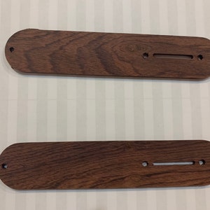 May include: Two wooden guitar pickguards with rounded edges and multiple holes for mounting. The pickguards are a dark brown color with a wood grain pattern.