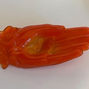 May include: Orange glass hand-shaped dish with a flower design.
