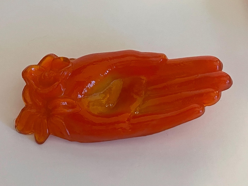 May include: Orange glass hand-shaped dish with a flower design.