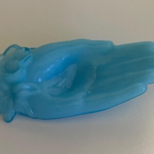 May include: A light blue glass hand-shaped dish with a flower design. The dish is made of frosted glass and has a vintage look.