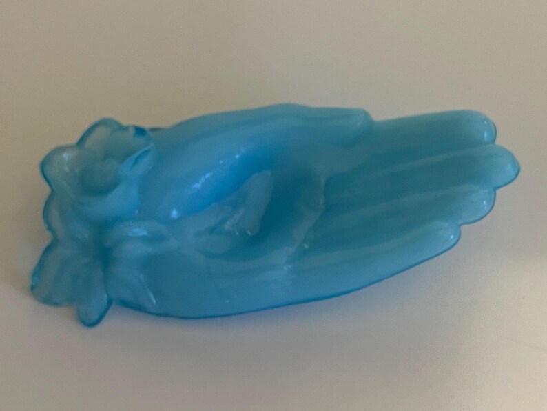May include: A light blue glass hand-shaped dish with a flower design. The dish is made of frosted glass and has a vintage look.