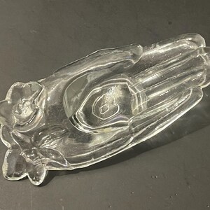 May include: A clear glass hand-shaped dish with a heart-shaped indentation in the palm. The dish has a floral design around the base.