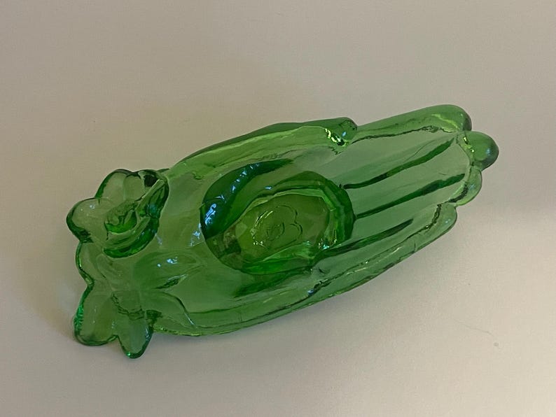 May include: A green glass hand-shaped dish with a raised design. The dish is perfect for holding small items like jewelry or trinkets.