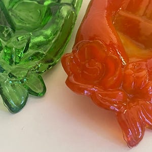May include: Two glass decorative items shaped like roses. One is green and the other is orange.