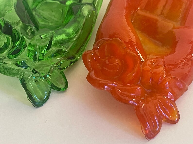 May include: Two glass decorative items shaped like roses. One is green and the other is orange.