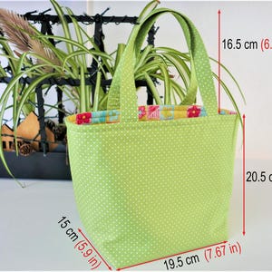 May include: A green fabric tote bag with white polka dots and a floral print lining. The bag has two handles and measures 16.5 cm tall, 20.5 cm wide, and 19.5 cm deep.