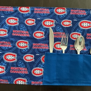 May include: A blue cutlery roll with a repeating pattern of the Montreal Canadiens logo and text. The roll contains a knife, fork, spoon, and teaspoon. The text reads "MONTREAL CANADIENS".
