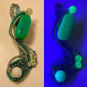 May include: A green stone pendant with a white stone and green glass beads, wrapped in silver and green wire. The pendant glows under a black light.