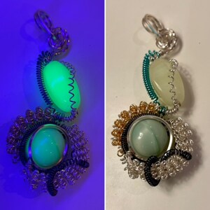 May include: A silver wire wrapped pendant with two green stones. The stones glow in the dark. The pendant is made with silver, gold, and black wire.