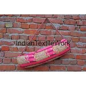 May include: A pink yoga mat bag with a brown strap and a tiger print design. The bag is hanging from a brick wall. The text "Indian TextileWork" is visible on the bag.