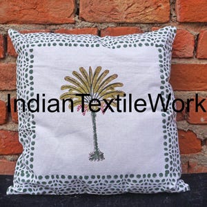 Puede incluir: Funda de almohada de algodón blanco con un borde de lunares verdes. La almohada presenta una impresión en bloque de una palmera estilizada en tonos de verde, amarillo y rosa.