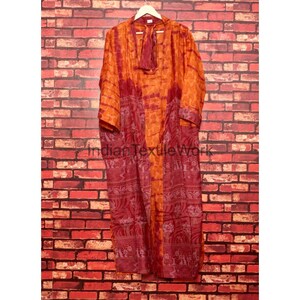 May include: A long, flowing robe in shades of orange and burgundy, hanging against a brick wall. The robe features a tie closure at the neck and a patterned design along the lower portion. The text "Indian Textile Work" is visible.