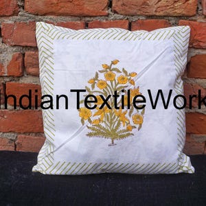 Puede incluir: Funda de cojín de algodón blanco con un borde de chevron verde y blanco. La funda de cojín presenta una impresión en bloque de flores amarillas con hojas verdes. El texto "Indian Textile Work" está impreso en negro en la funda de cojín.