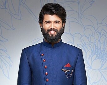 Könnte beinhalten: Ein Mann trägt eine blaue, langärmelige Kurta mit weißer Hose und schwarzen Schuhen. Die Kurta hat einen Stehkragen und einen Knopfverschluss. Der Mann steht vor einem floralen Hintergrund.