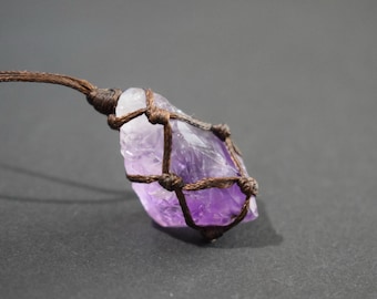 May include: A raw amethyst crystal pendant, showcasing a gradient of purple hues. The crystal is encased in a woven brown cord, creating a natural and earthy aesthetic. The pendant is suspended from a matching brown cord.