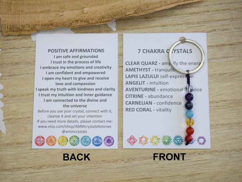 May include: A white card with the text "POSITIVE AFFIRMATIONS" and a list of affirmations.  The card is next to a white card with the text "7 CHAKRA CRYSTALS" and a list of crystals and their meanings.  A silver key chain with seven colored beads is attached to the card.