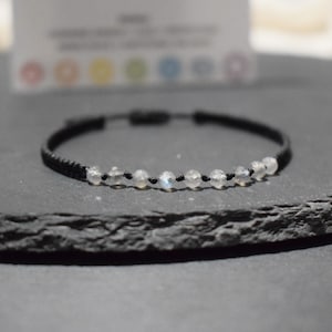 Peut inclure: Un bracelet en cordon noir avec une rangée de perles de pierre de lune blanche.