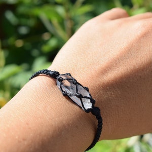 May include: A black cord bracelet with a clear quartz crystal wrapped in a macrame knot.