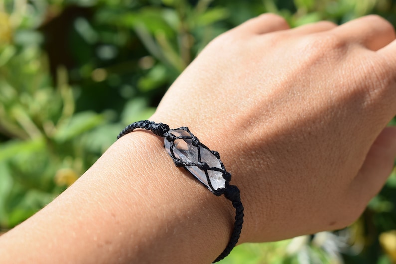 May include: A black cord bracelet with a clear quartz crystal wrapped in a macrame knot.