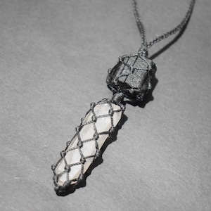May include: A black cord necklace with a black crystal and a clear crystal wrapped in macrame.