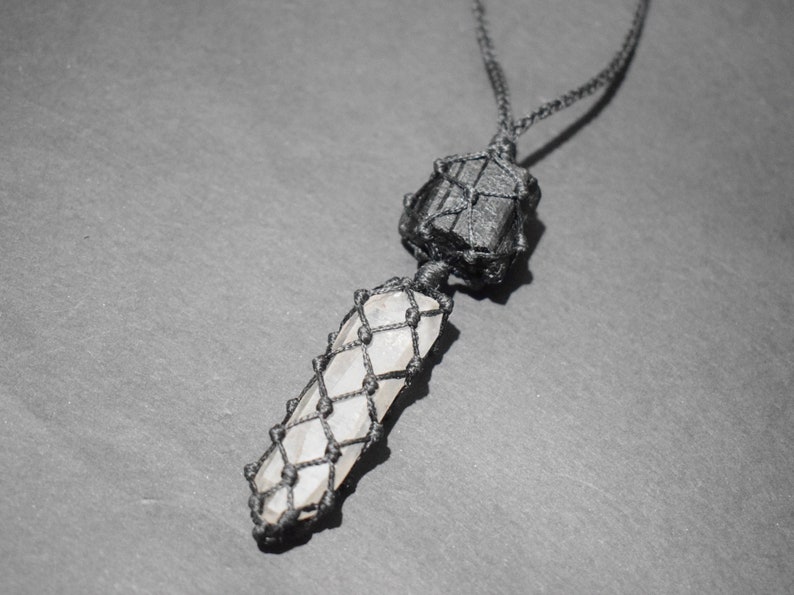 May include: A black cord necklace with a black crystal and a clear crystal wrapped in macrame.