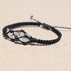 May include: A black cord bracelet with a clear quartz crystal wrapped in the cord.