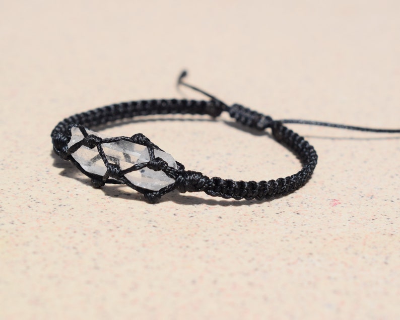 May include: A black cord bracelet with a clear quartz crystal wrapped in the cord.