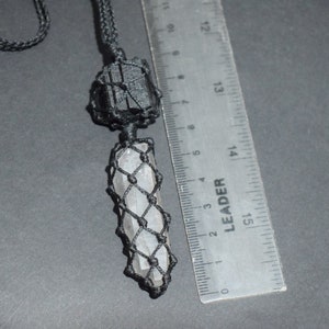 May include: A black cord necklace with a clear crystal pendant wrapped in black macrame. The crystal is about 5 cm long and is next to a ruler for size reference.