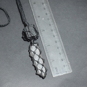 May include: A black cord necklace with a clear crystal point pendant wrapped in black macrame. The crystal is about 4 inches long and the macrame is about 5 inches long. The necklace is next to a ruler for size reference.