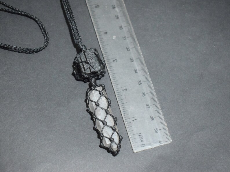 May include: A black cord necklace with a clear crystal point pendant wrapped in black macrame. The crystal is about 4 inches long and the macrame is about 5 inches long. The necklace is next to a ruler for size reference.