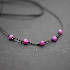 Puede incluir: Un collar sencillo con un cordón negro y cinco cuentas de piedras preciosas rosas.