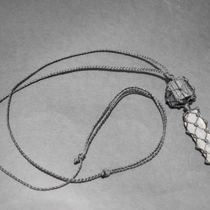 May include: A black cord necklace with a crystal pendant wrapped in black cord. The crystal is a light gray color and has a rough, natural texture.