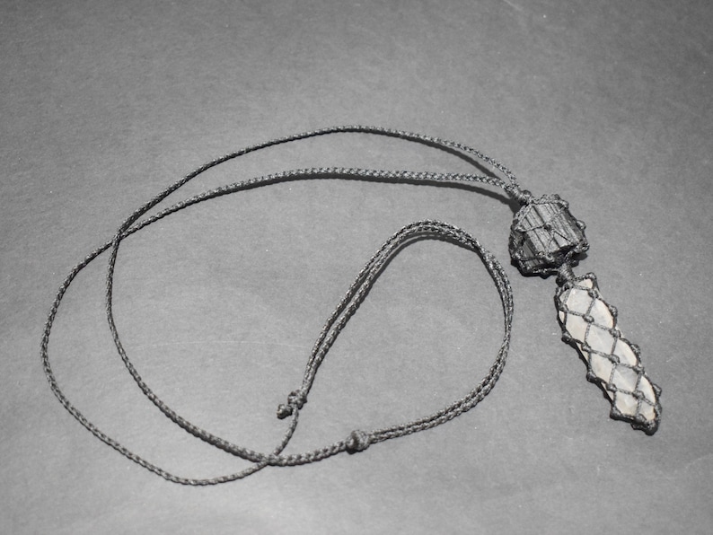 May include: A black cord necklace with a crystal pendant wrapped in black cord. The crystal is a light gray color and has a rough, natural texture.