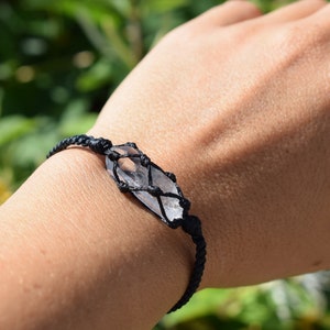 May include: A black cord bracelet with a clear crystal wrapped in the cord. The bracelet is on a person's wrist.