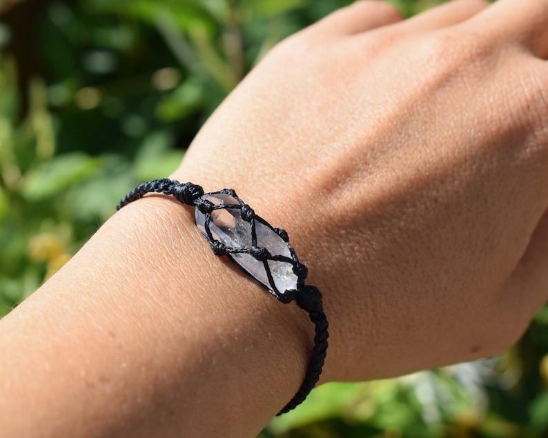 May include: A black cord bracelet with a clear crystal wrapped in the cord. The bracelet is on a person's wrist.