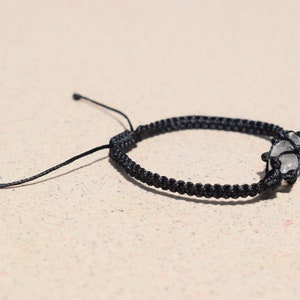 May include: A black braided bracelet with a clear crystal charm.