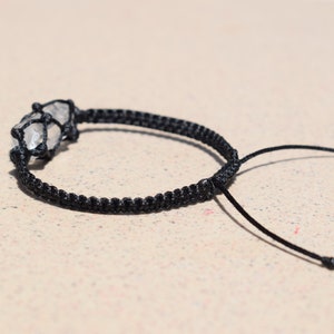 May include: A black cord bracelet with a clear quartz crystal wrapped in the cord.