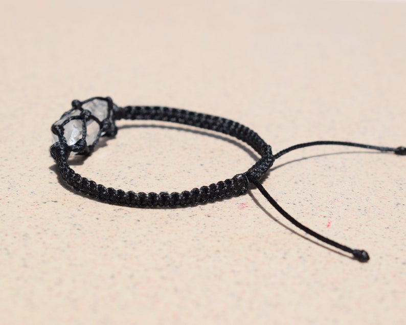 May include: A black cord bracelet with a clear quartz crystal wrapped in the cord.
