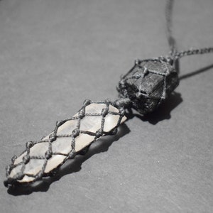 May include: A black cord necklace with a clear crystal pendant wrapped in black cord and a black stone pendant also wrapped in black cord.