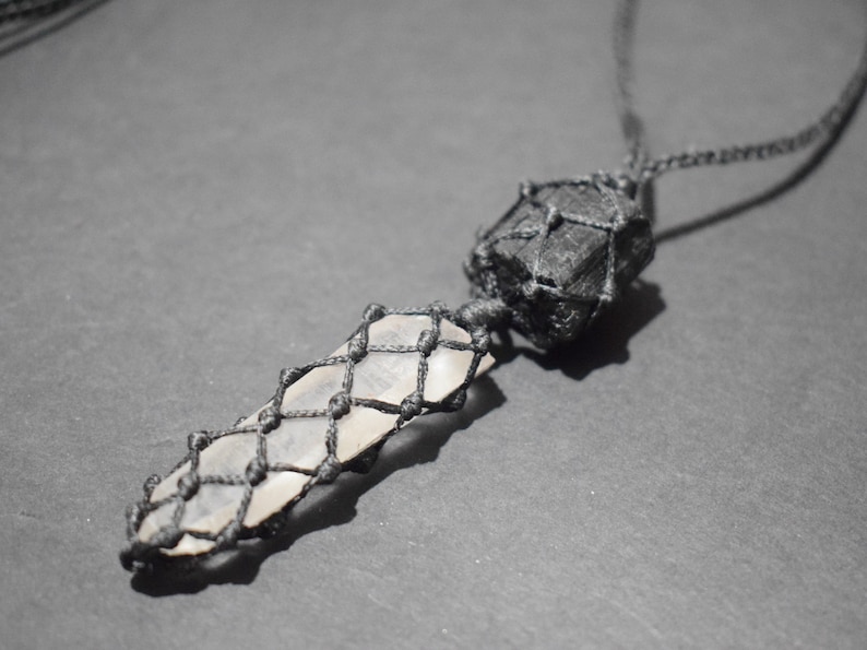 May include: A black cord necklace with a clear crystal pendant wrapped in black cord and a black stone pendant also wrapped in black cord.