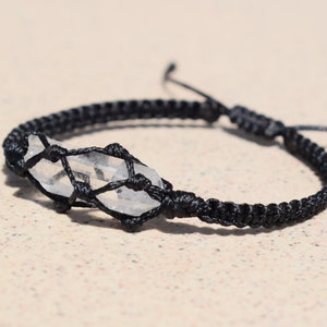 May include: A black cord bracelet with a clear quartz crystal wrapped in a macrame knot.
