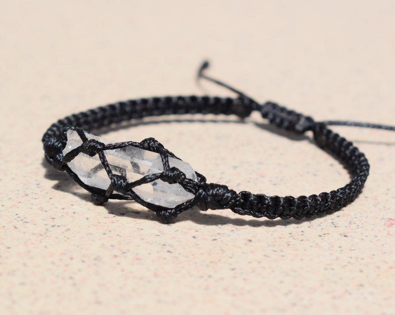 May include: A black cord bracelet with a clear quartz crystal wrapped in a macrame knot.